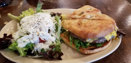 A plate with a cheeseburger on a bun and a side salad topped with ranch dressing and pepper.