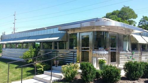 A shiny, silver diner with large windows and a welcoming entrance, surrounded by green landscaping on a sunny day.