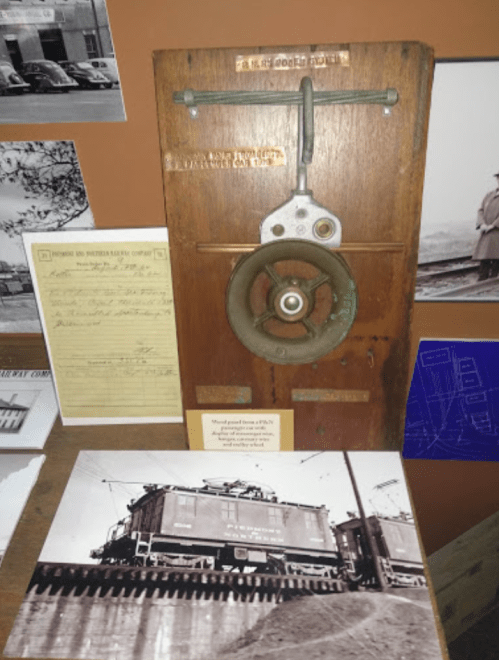 A wooden display featuring a vintage pulley, historical photos, and documents related to a railway company.