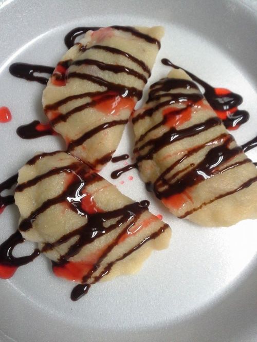 Three dumplings drizzled with chocolate and red sauce on a white plate.