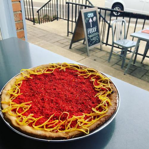A colorful pizza topped with red seasoning and yellow strips, displayed on a table with an outdoor view.