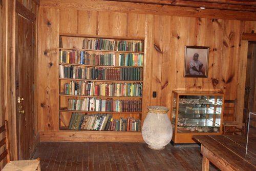 A cozy wooden room featuring a bookshelf filled with books, a display case, and a framed portrait on the wall.