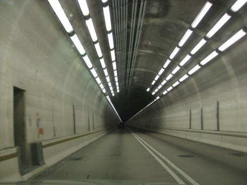 A view inside a long, illuminated tunnel with smooth concrete walls and a road leading into the distance.