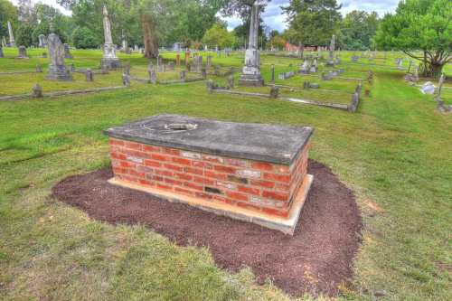 A brick burial vault surrounded by grass in a cemetery, with gravestones visible in the background.