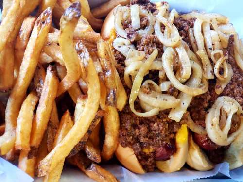 A plate featuring a chili dog topped with onions and a side of golden, crispy French fries.