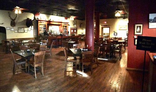 A dimly lit restaurant interior with wooden tables, chairs, and a bar in the background, featuring rustic decor.