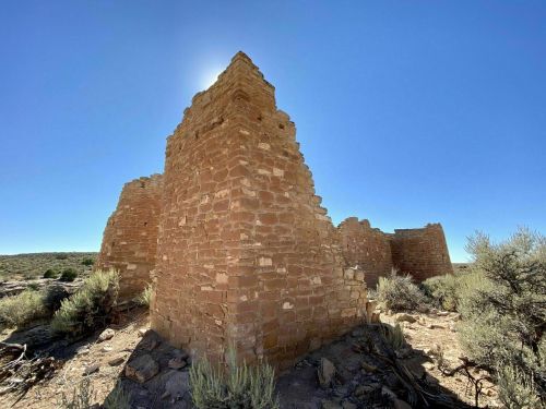 Ruins of a stone structure under a clear blue sky, surrounded by sparse vegetation and rocky terrain.