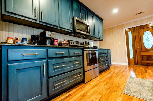 A modern kitchen with blue cabinets, stainless steel appliances, and wooden flooring, featuring a cozy entrance door.