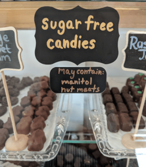 Display of sugar-free candies with a sign noting potential manitol and nut meat content.