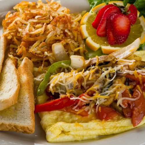 A hearty breakfast plate with an omelet, hash browns, toast, and fresh fruit including strawberries and orange slices.