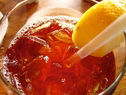 Close-up of a glass filled with iced tea, ice cubes, and a slice of lemon on the rim.