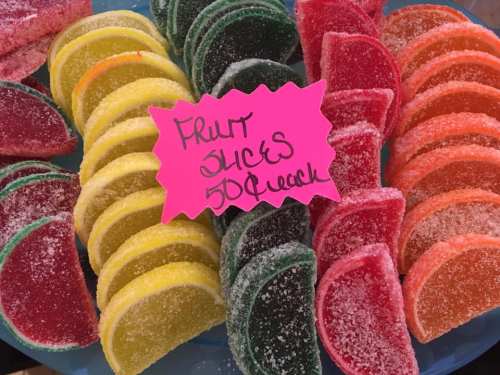 Colorful fruit slice candies arranged on a blue plate, with a bright pink sign reading "Fruit Slices 50¢ each."