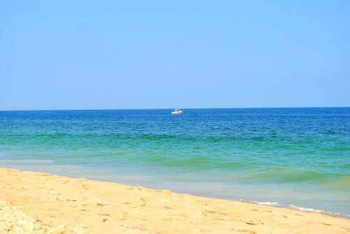 A serene beach scene with golden sand and calm blue-green waters, featuring a small boat in the distance.