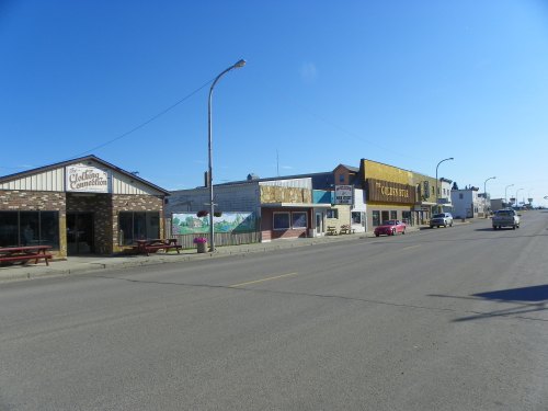 A quiet street scene featuring small businesses and shops under a clear blue sky.