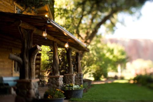 A rustic log cabin with a porch, surrounded by greenery and flower pots, set in a serene outdoor environment.
