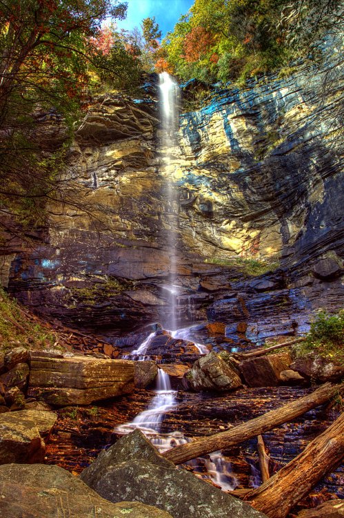 A stunning waterfall cascades down rocky cliffs, surrounded by vibrant autumn foliage and serene natural scenery.