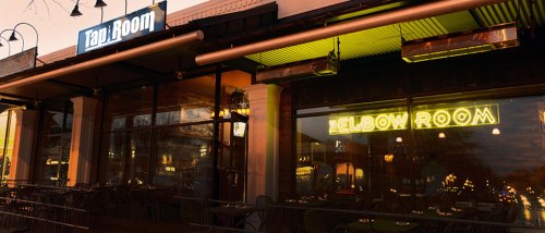 Exterior view of a restaurant with neon signs for "Tabi Room" and "The Elbow Room" during sunset.