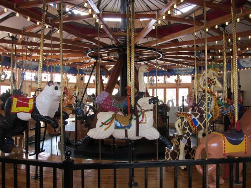 A colorful carousel featuring various animal figures, including a panda, horse, and giraffe, under bright lights.
