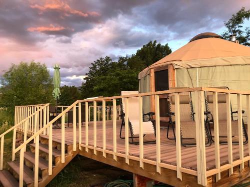 A wooden deck with chairs leads to a yurt, surrounded by trees and a colorful sunset sky.