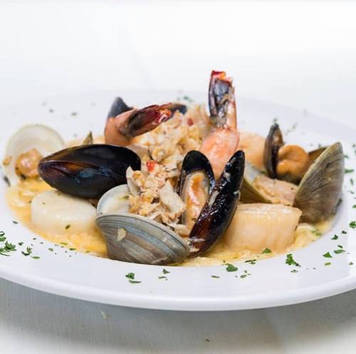 A plate of seafood pasta featuring shrimp, mussels, clams, and scallops, garnished with parsley.