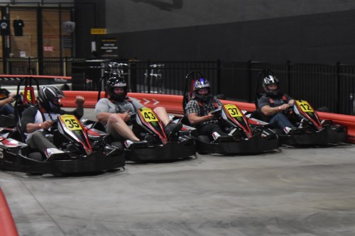 Four go-karts lined up on a track, with drivers wearing helmets, ready to race.