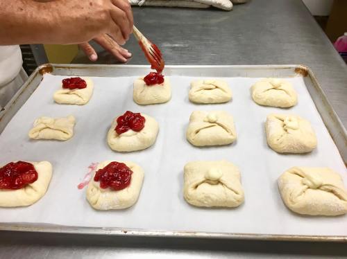 A baker adds cherry filling to dough squares on a baking sheet lined with parchment paper.