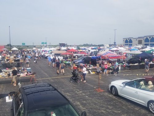 A bustling outdoor flea market with numerous tents, vendors, and shoppers exploring various goods.