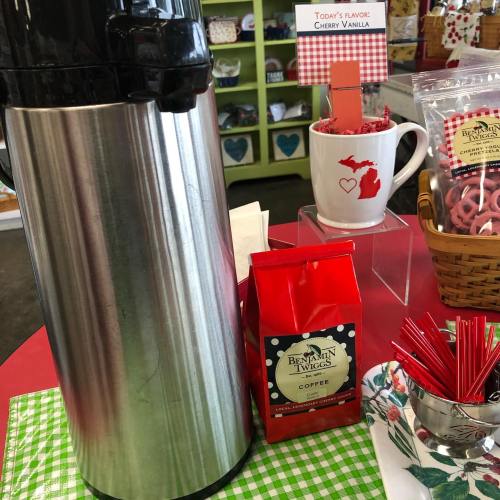 A stainless steel coffee dispenser next to a bag of cherry vanilla coffee and a decorative mug on a red table.