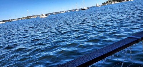 A serene view of a calm blue sea with sailboats in the distance under a clear blue sky.