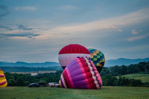 Colorful hot air balloons on a grassy field with mountains and a cloudy sky in the background.