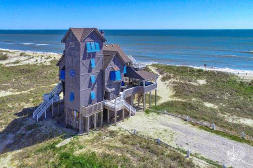A unique beach house with blue shutters, elevated on stilts, overlooking the ocean and sandy dunes.