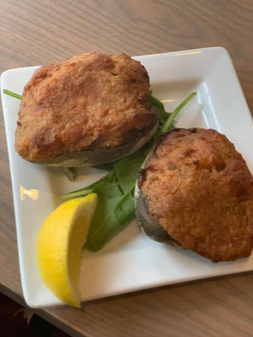 Two golden-brown fried items on a white plate, garnished with a lemon wedge and leafy greens.