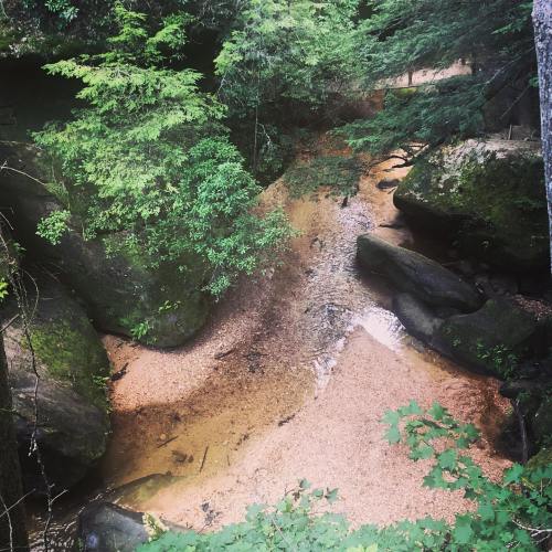 A serene river winding through lush greenery and rocky banks, with sandy areas visible along the water's edge.