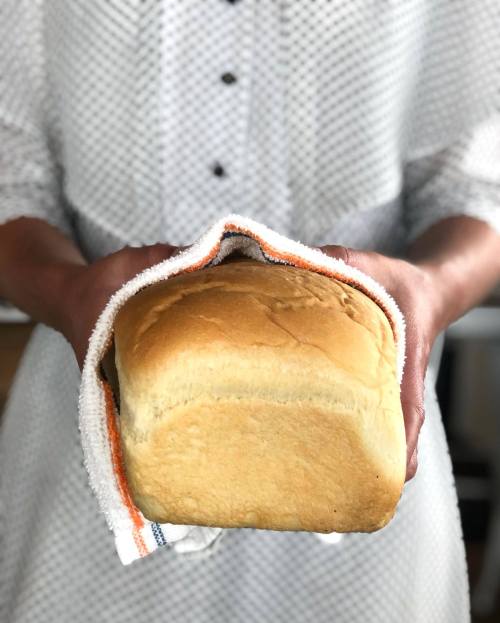 A person holds a freshly baked loaf of bread wrapped in a kitchen towel.