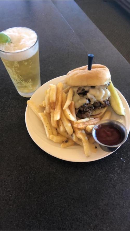A plate with a cheeseburger, fries, a pickle, and a small cup of ketchup, alongside a glass of soda.