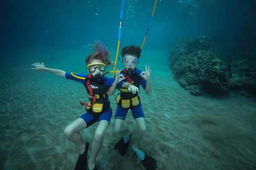 Two children in snorkeling gear underwater, smiling and posing with colorful fins and a vibrant marine backdrop.