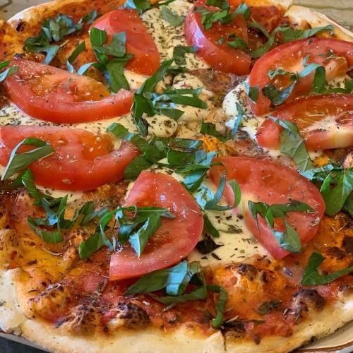 A freshly baked pizza topped with sliced tomatoes, fresh basil, and mozzarella cheese on a golden crust.