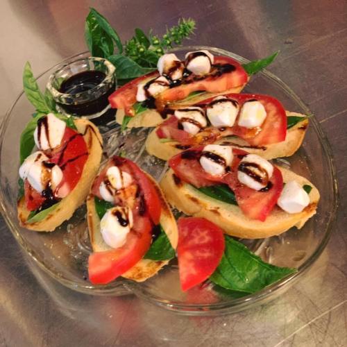 A plate of bruschetta topped with tomatoes, mozzarella, basil, and balsamic glaze, served with a small dish of balsamic.