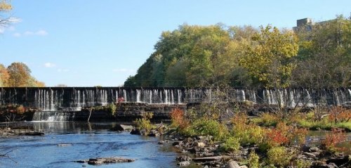 A serene landscape featuring a waterfall cascading over a dam, surrounded by trees and colorful autumn foliage.