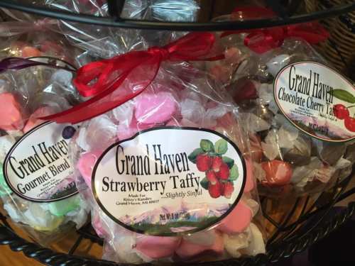 Bags of colorful taffy candies labeled "Grand Haven" in a display basket, featuring strawberry and chocolate cherry flavors.