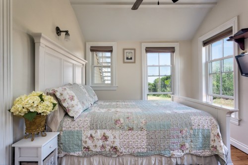 Cozy bedroom with a floral quilt, white furniture, and large windows letting in natural light.
