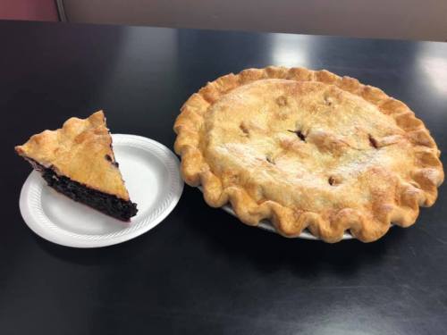 A whole pie next to a slice on a plate, both featuring a golden-brown crust and a dark filling.