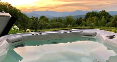 A hot tub overlooking a scenic landscape at sunset, with mountains and trees in the background.