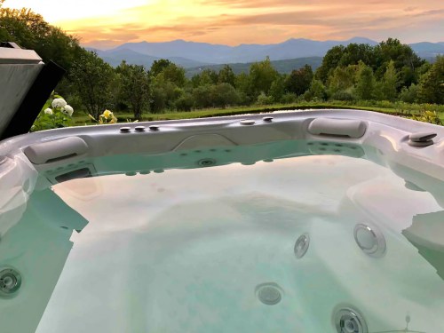 A hot tub overlooking a scenic landscape with mountains and trees at sunset.