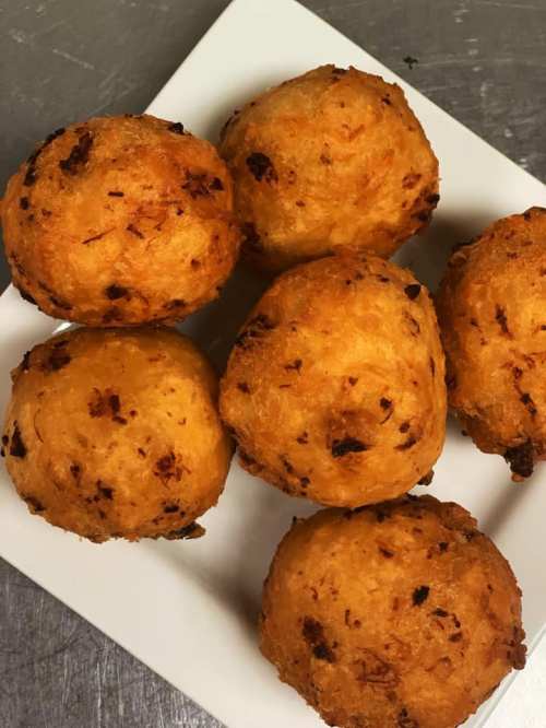 A plate of six golden-brown, round fritters with a crispy exterior and a slightly textured surface.