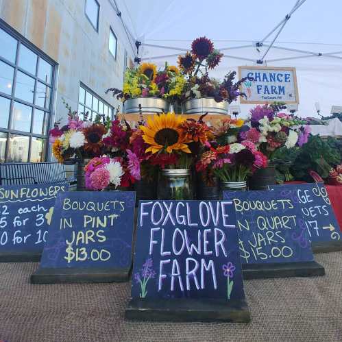 A vibrant flower stand at a market featuring colorful bouquets and signs for pricing, under a white tent.