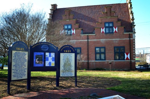 Historic building with a red-tiled roof, flanked by informational signs in a grassy area.