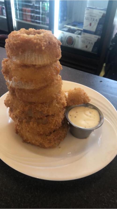 A stack of crispy fried onion rings served with a small cup of dipping sauce on a white plate.