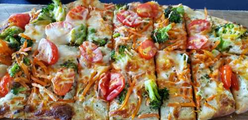 A freshly baked vegetable pizza topped with broccoli, tomatoes, and shredded carrots on a wooden serving board.