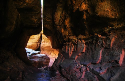 A narrow canyon with towering rock walls, illuminated by light streaming through a gap at the top.